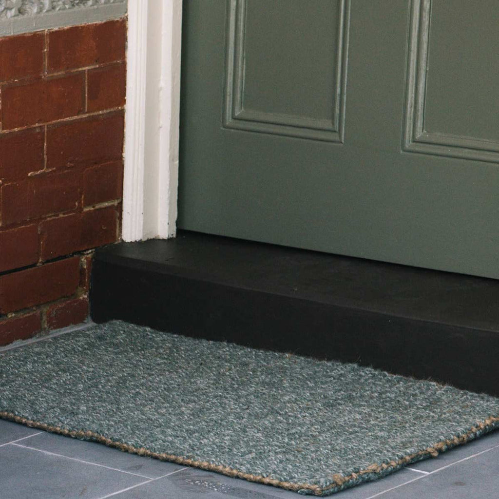 A doorway with a sage green entrance mat, made from wool and jute. 