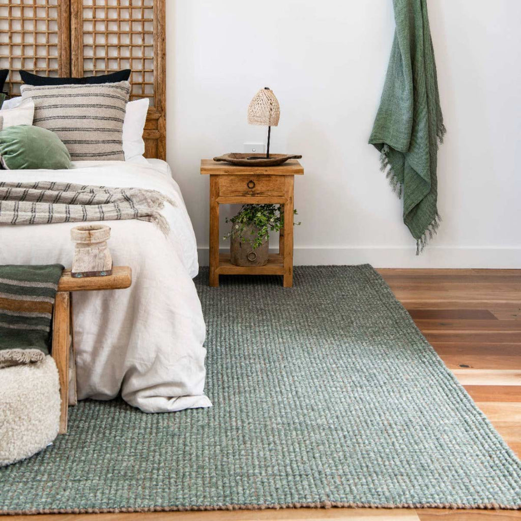 A bedroom decorated in shades of green and white, with a green floor rug made with organic wool and jute. 