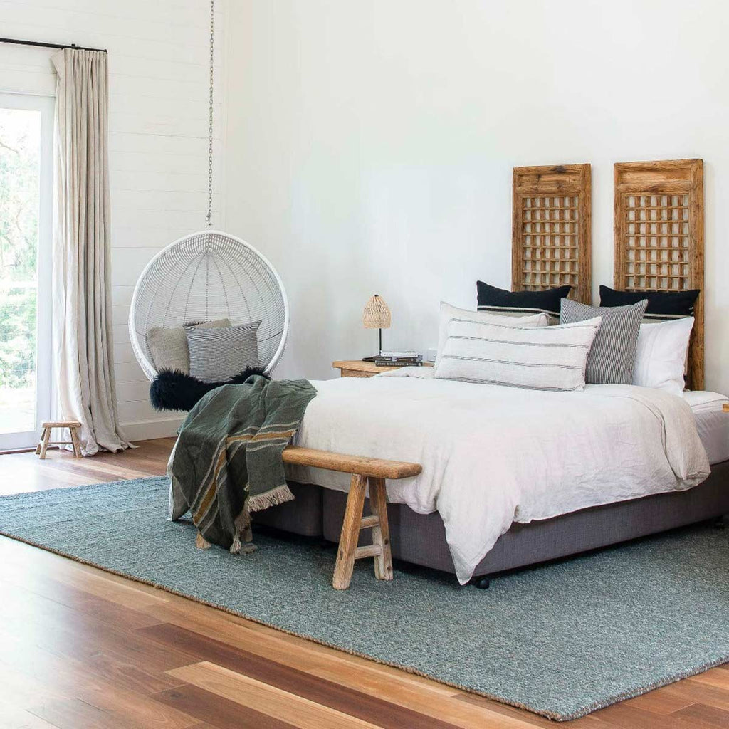 A simple, minimalist bedroom with a large floor rug made of natural jute and wool, in a muted sage green shade. 