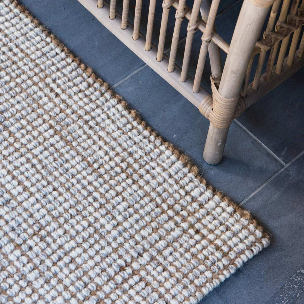 A corner image of a bohemian style floor rug, woven in a boucle style with cream and grey wool and natural brown jute fibres. 