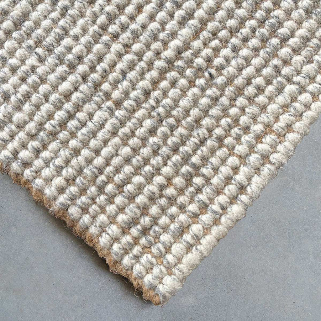 A corner view of a cream and natural brown wool and jute floor rug. 