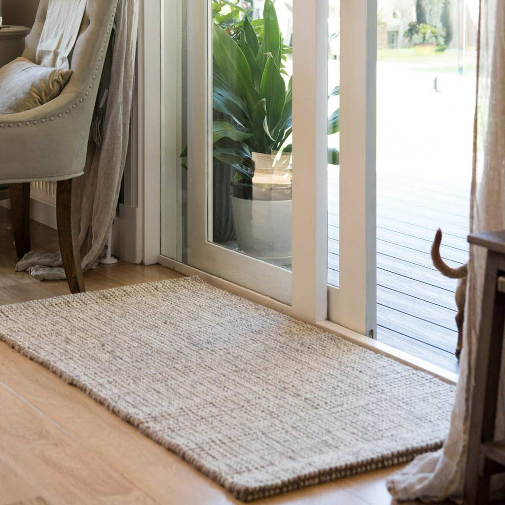 A large and durable entrance mat made from jute and wool in shades of white and brown sits in a doorway. 