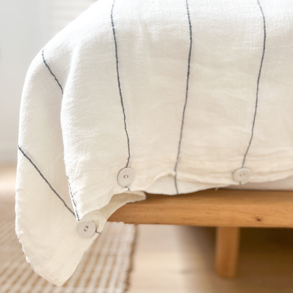 Detail of the button closures of the French flax linen duvet cover in white with a fine charcoal line pattern. 