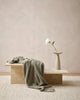 Baya cotton blend throw blanket in a muted olive green, draped on a table in a contemporary home