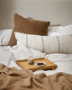 The Baya cyprian cushion in cocoa brown decorating a bed