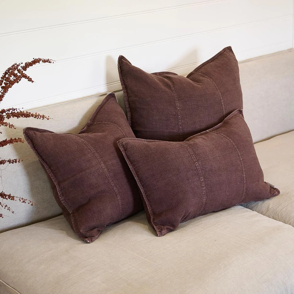 Three Eadie Lifestyle Luca linen cushions in Chocolate on a linen sofa with dried stems.