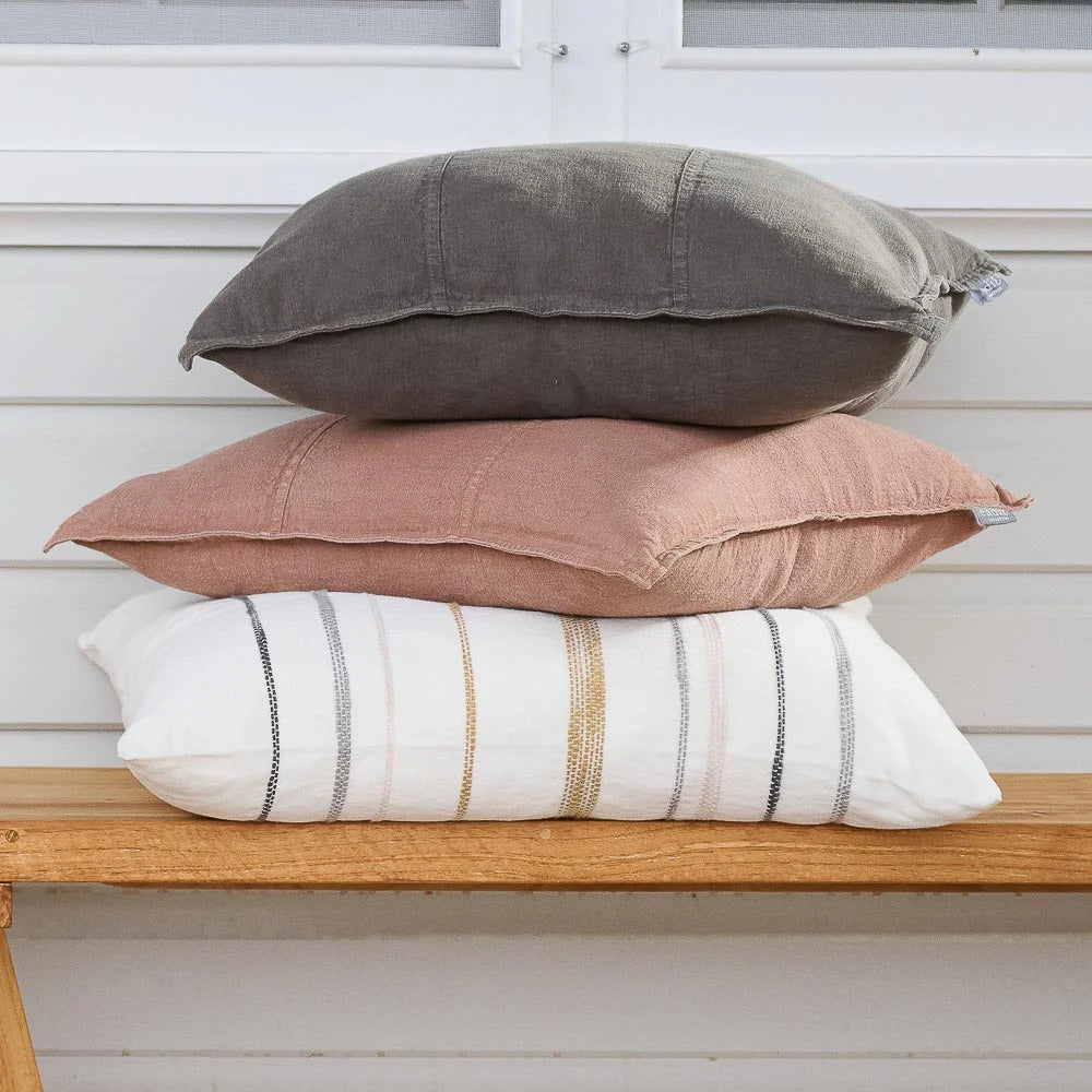 Luca linen cushions stacked on a timber bench with a charcoal cushion and a striped lumbar.