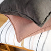 Close view of a Luca linen cushion in Clay layered under a charcoal cushion on a timber bench.