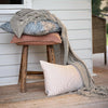 Cushions and a knitted throw on a timber stool on a verandah, with a Luca cushion in Clay.