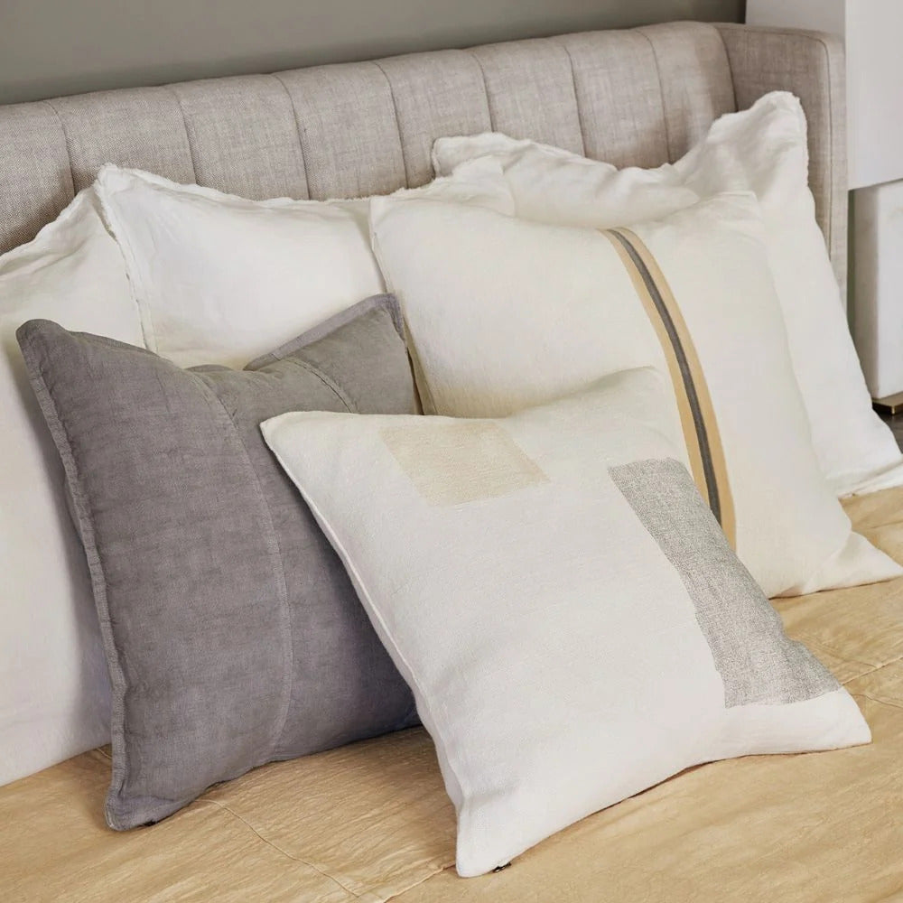 Eadie Lifestyle Luca linen cushion in Grey layered on a bed with white linen cushions.