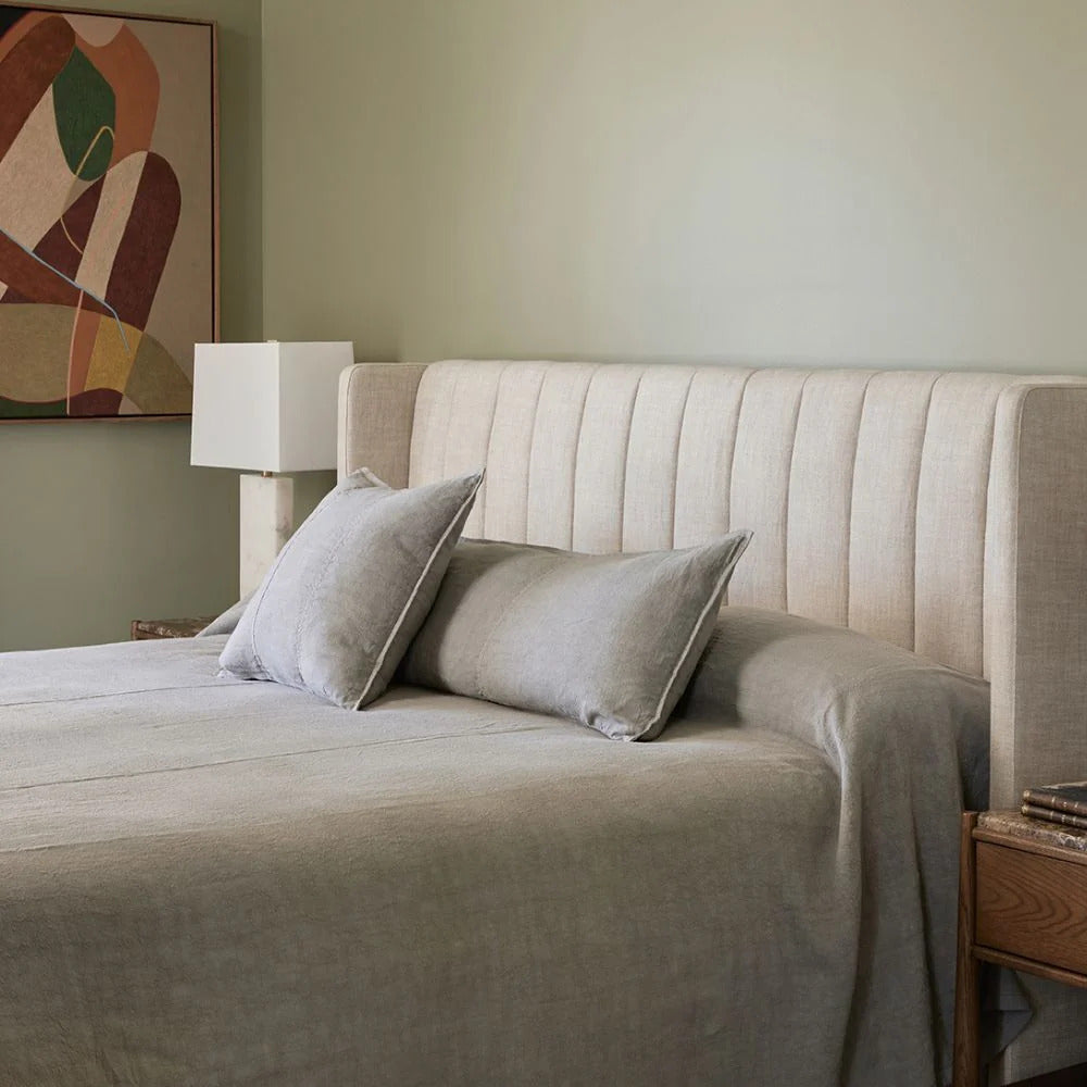 Grey linen cushions and bedding on a bed against a soft green wall.