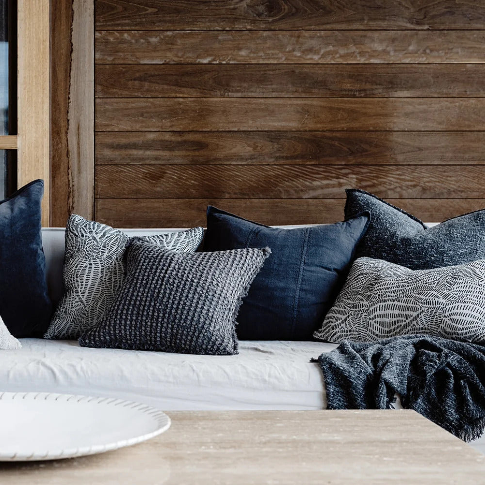 Eadie Lifestyle Luca linen cushion in Midnight on a sofa against a timber wall with dark cushions.