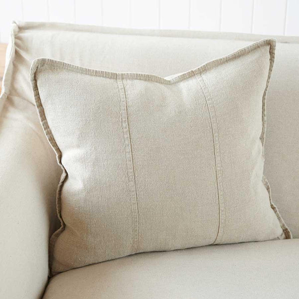 Eadie Lifestyle Luca linen cushion in Natural on a cream sofa against a white panelled wall.