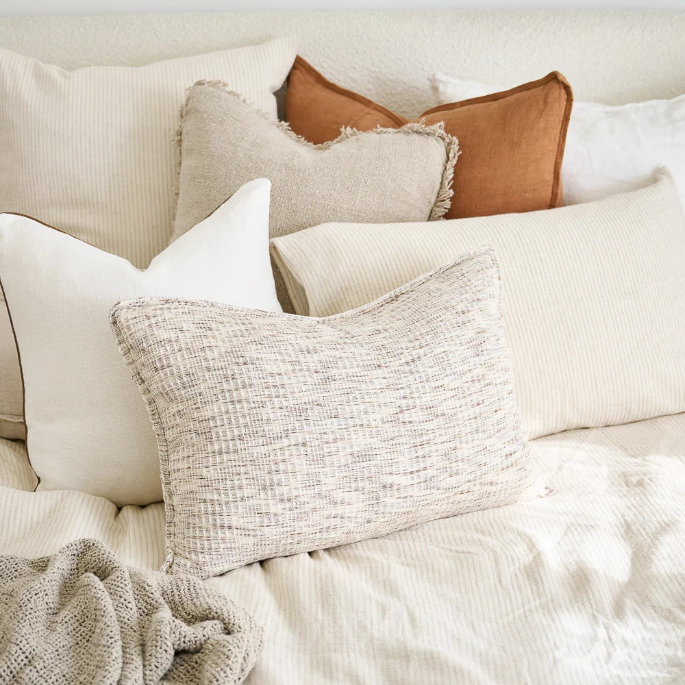 Layered linen cushions on a bed, with a Luca cushion in Nutmeg at the back.