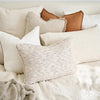 Layered linen cushions on a bed, with a Luca cushion in Nutmeg at the back.