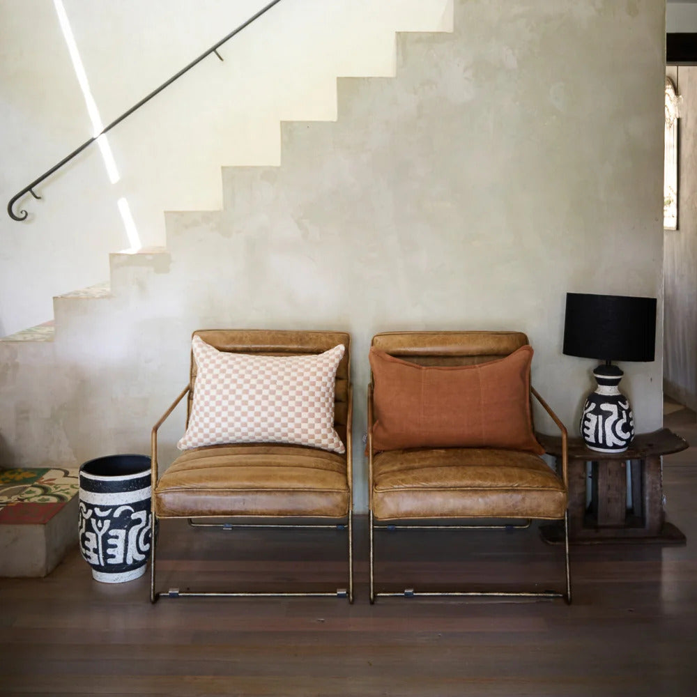 Two tan leather chairs with a Luca linen cushion in Nutmeg and a checked cushion.