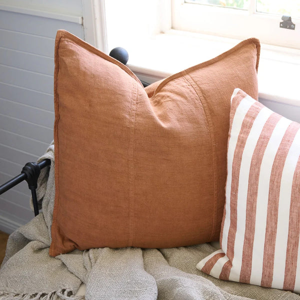 Eadie Lifestyle Luca linen cushion in Nutmeg on a window seat beside a striped cushion.