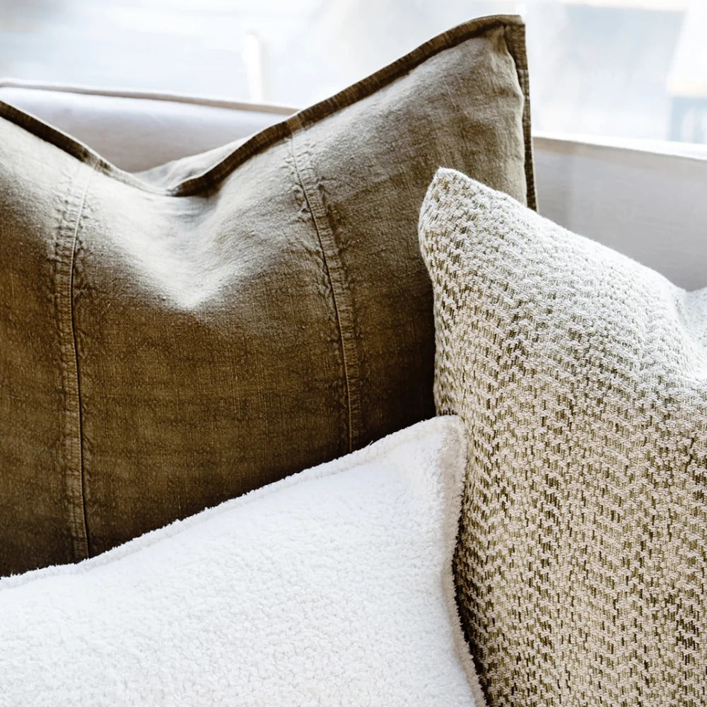 Eadie Lifestyle Luca linen cushion in Olive beside a white bouclé cushion in window light.