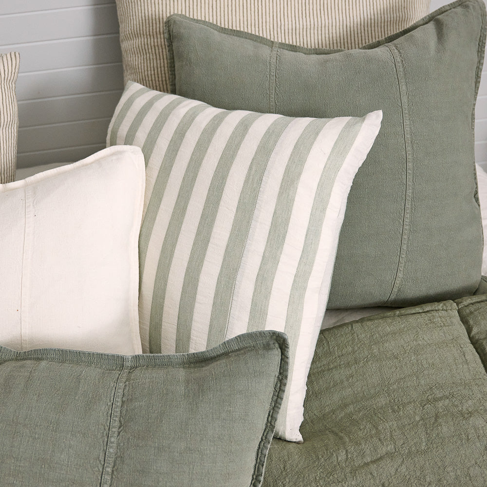 Luca linen cushions in Pistachio layered on a bed with striped and white cushions.