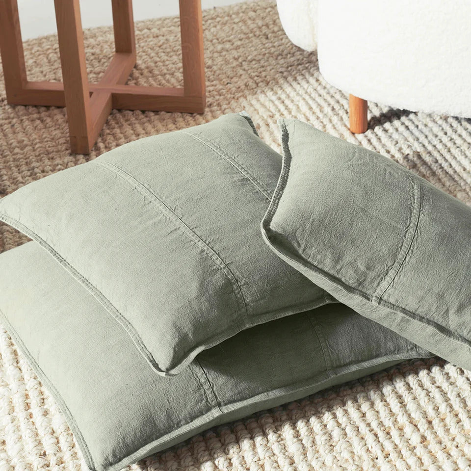 Two Eadie Lifestyle Luca linen cushions in Pistachio resting on a woven jute rug.