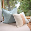 Eadie Lifestyle Luca linen cushion in Sky on a window seat beside a striped cushion.