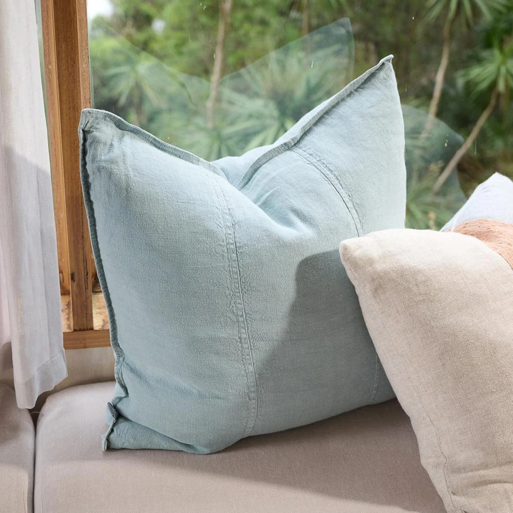 Eadie Lifestyle Luca linen cushion in Sky on a window seat with greenery beyond.
