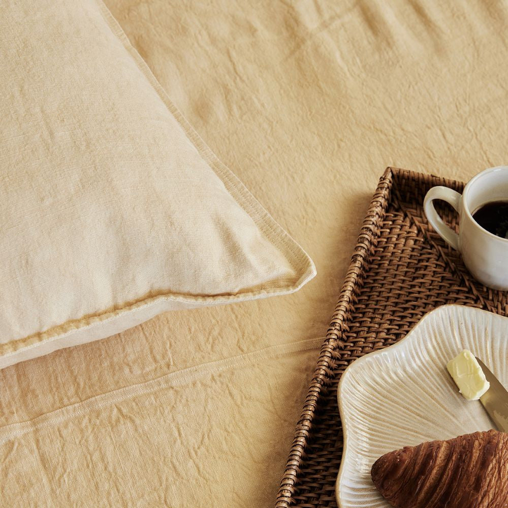 Eadie Lifestyle Luca linen cushion in Soft Butter on a bed with a breakfast tray.