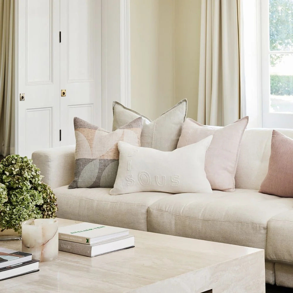 Eadie Lifestyle Luca linen cushion in Soft Lilac on a pale linen sofa with layered neutral cushions.