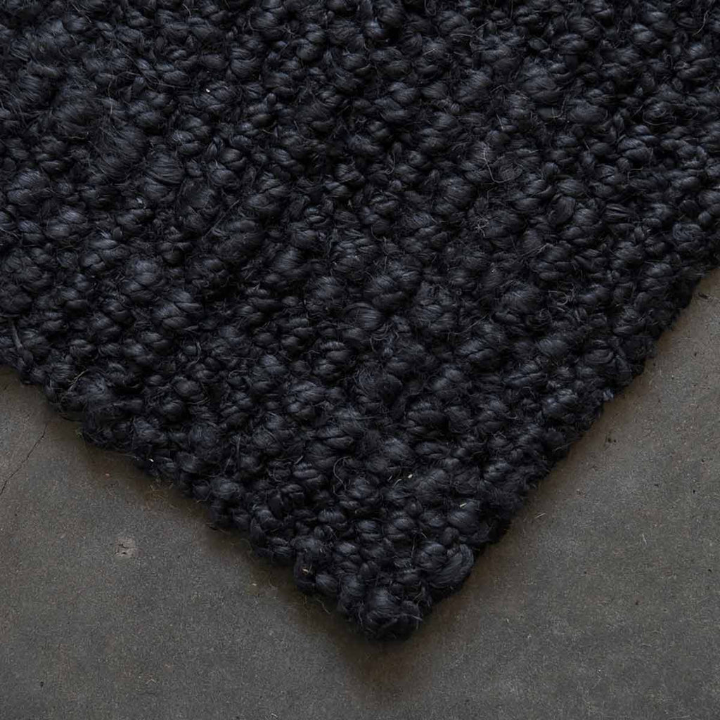 A corner view of a textured black jute floor rug. 