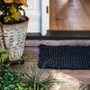 A doorway with a black jute entrance mat, handwoven in a textural boucle style. 