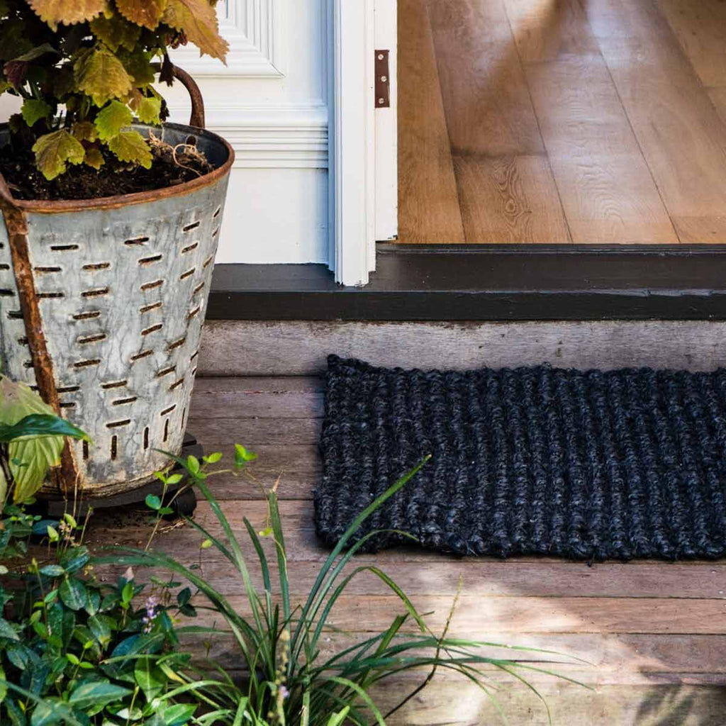 A doorway with a black jute entrance mat, handwoven in a textural boucle style. 