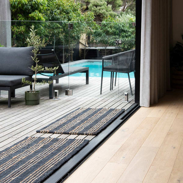 A deck with two large mats hand knotted with natural jute fibres in a black and natural brown striped pattern. 