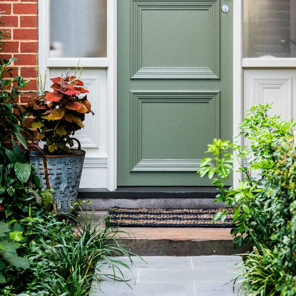A door with a knotted doormat in natural jute, with black and brown stripes. 