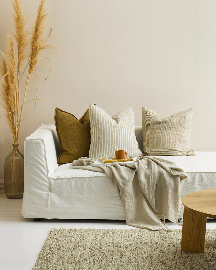 Three Baya linen cushions in warm earthy tones on a cream couch 