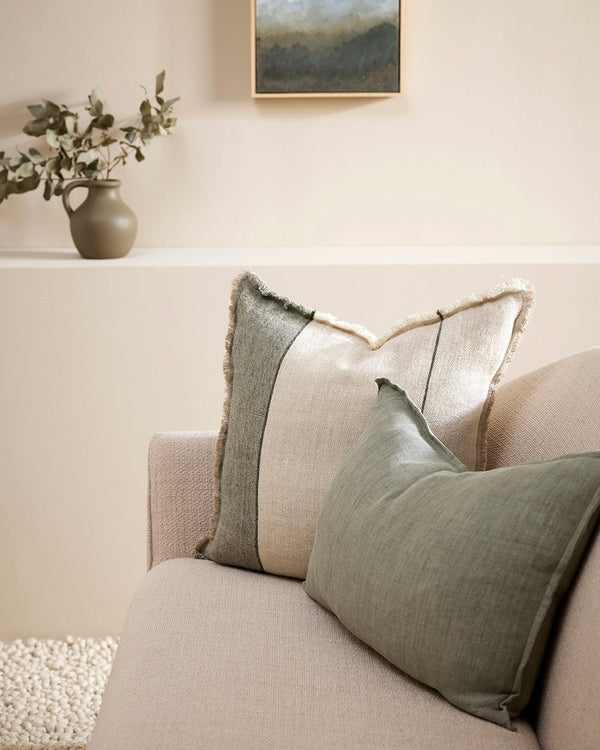 A natural linen cushion with sage green stripe and fringed edge detail, seen on a couch with a complementary green cushion