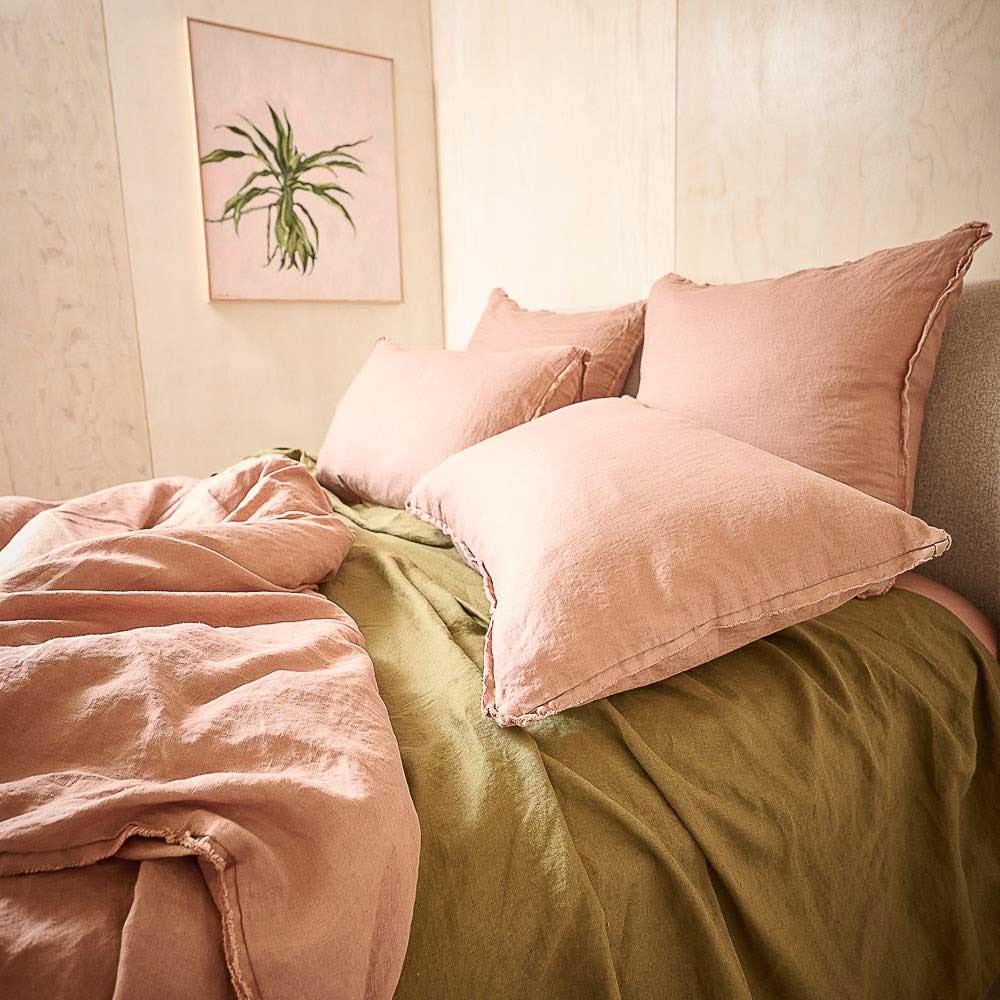 A gorgeous bed in a stylish, sunny bedroom. The bed is made up with French flax linen bedding, with pillows and duvet cover in a gorgeous lotus pink colour, and the flat sheet in a contrasting olive green, lending sophistication and charm. 