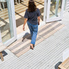 A woman walks into an entryway over two neutral beige coloured doormats, both with striping details in a blue grey tone. 