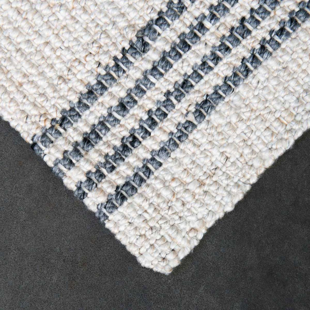 A detailed view of the corner of a 100% PET entrance mat, in natural beige with slate stripe. 
