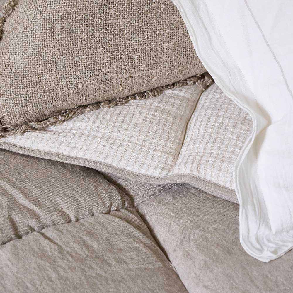 A close up image of the Marina bedcover with natural beige toned stripes on one side, and a neutral block on the other. 