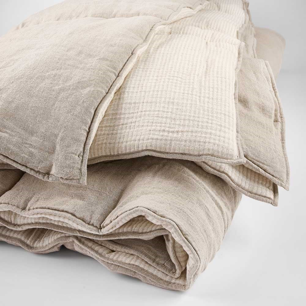 A folded bed cover, with quilted insets, one side being flat-block taupe and one being a creamy pinstripe. 