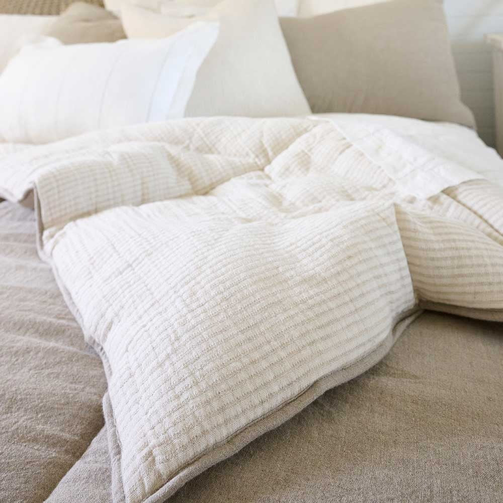 A corner image of the Marina bedcover by Eadie Lifestyle, showing off the taupe block outer and the inner of sweet cream and soft beige stripes. 