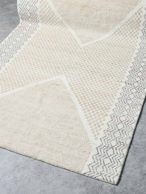 A stunning hand-knotted wool rug by Tribe Home. A geometric pattern in ivory and soft pink runs across the middle and sides, highlighting the artistry of the weaving.