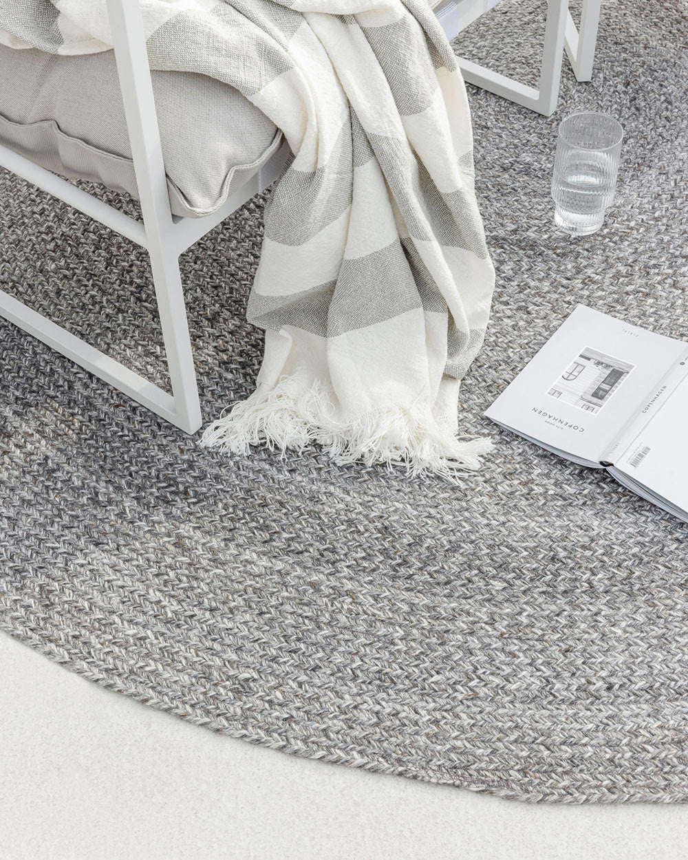 Detailed view of chair and book atop a grey-toned PET recycled fibre outdoor rug by Baya NZ