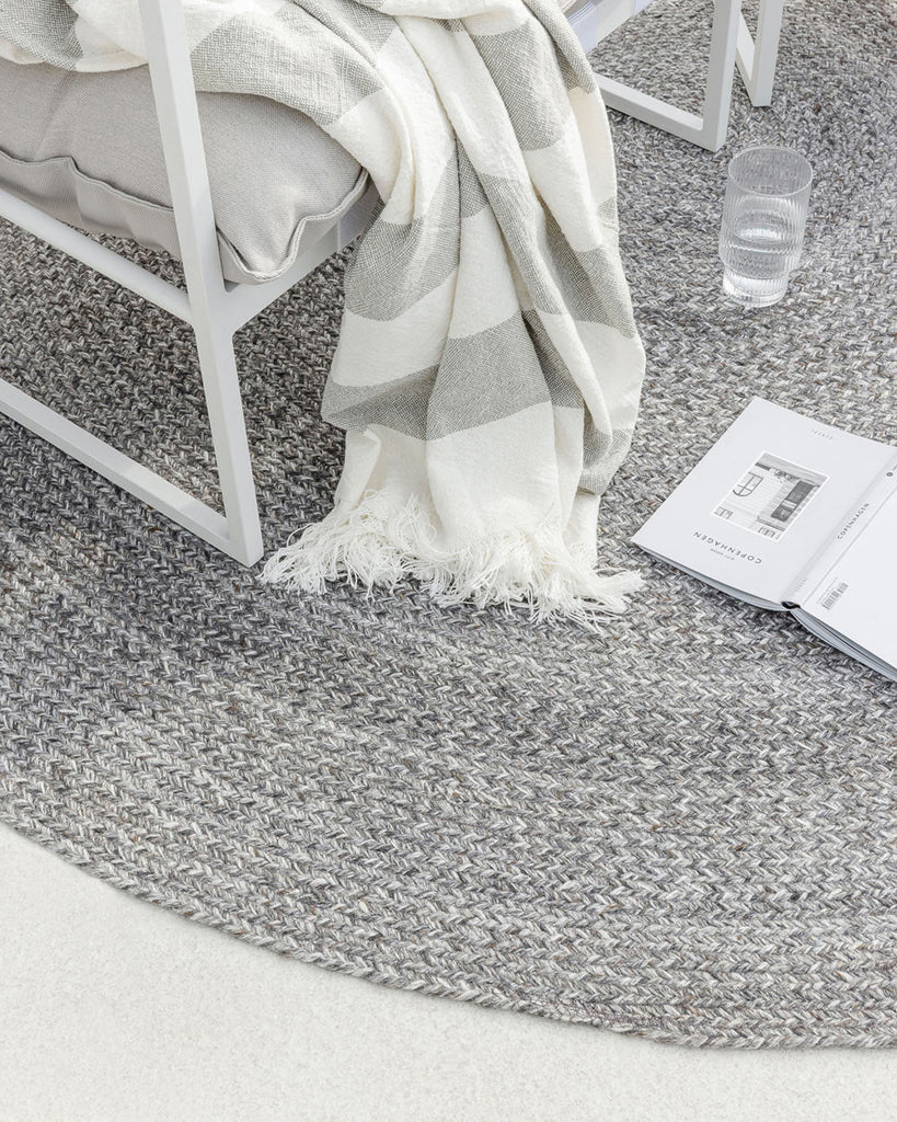 Detailed view of chair and book atop a grey-toned PET recycled fibre outdoor rug by Baya NZ