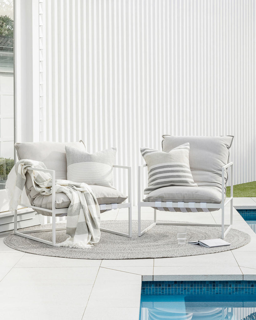Baya NZ's round outdoor rug in grey tones in situation outside a pool with two chairs sitting atop it. 