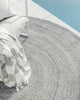 An outdoor rug by Baya NZ in cool grey tones, sitting outside by a blue swimming pool. 