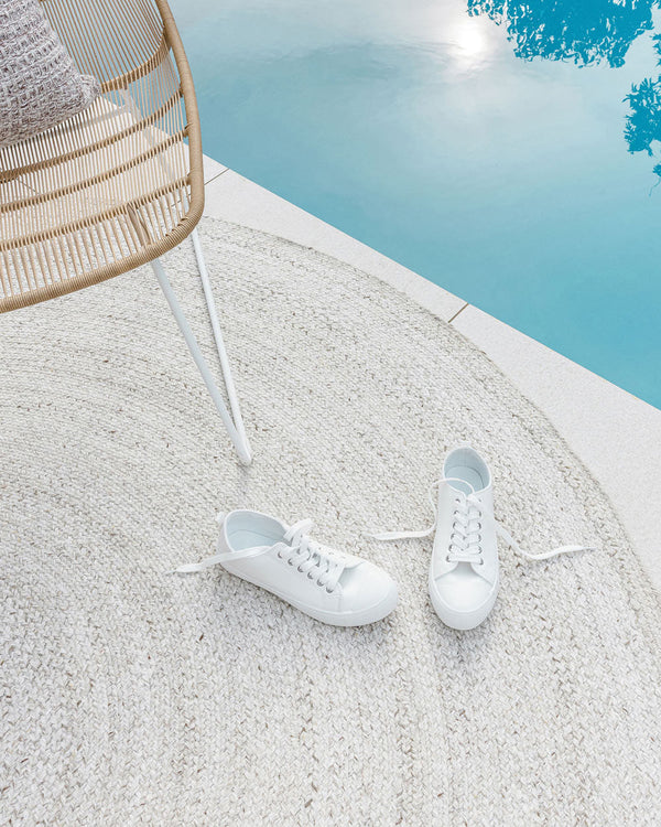 An outdoor rug in shades of cool white by Baya NZ, sitting by a swimming pool with a pair of white shoes on top of it. 