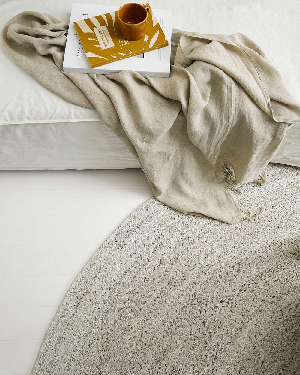 A cool white rug by Baya NZ depicted inside next to a couch, with a beige throw also by Baya NZ. 