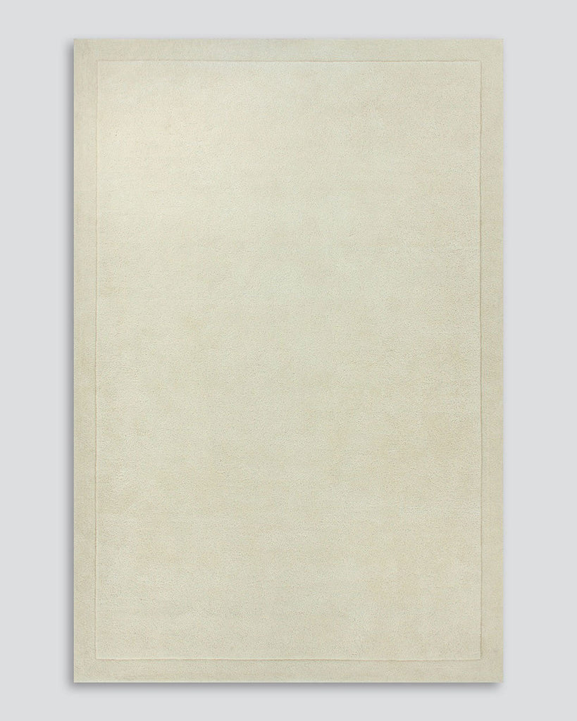 A full image of the Norfolk floor rug in the shade Ivory. The border of the rug is cut-pile in a minimalist and refined design, and the pile of the rug's centre is luxuriously deep.
