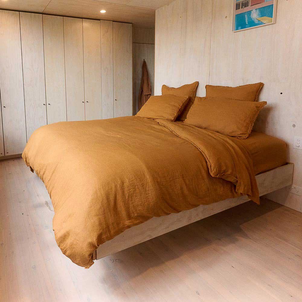 A gorgeous minimalistic bedroom with a monochromatic bed in the centre, dressed in all ochre, French flax linen bedding. 